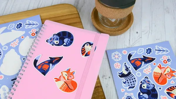 An open animal-themed friend book with watercolor illustrations and a child's handwritten message on cream pages, surrounded by colored pencils on a wooden table